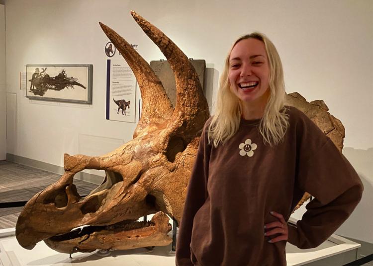 Rachel Shea standing in front of triceratops skull in paleontology hall