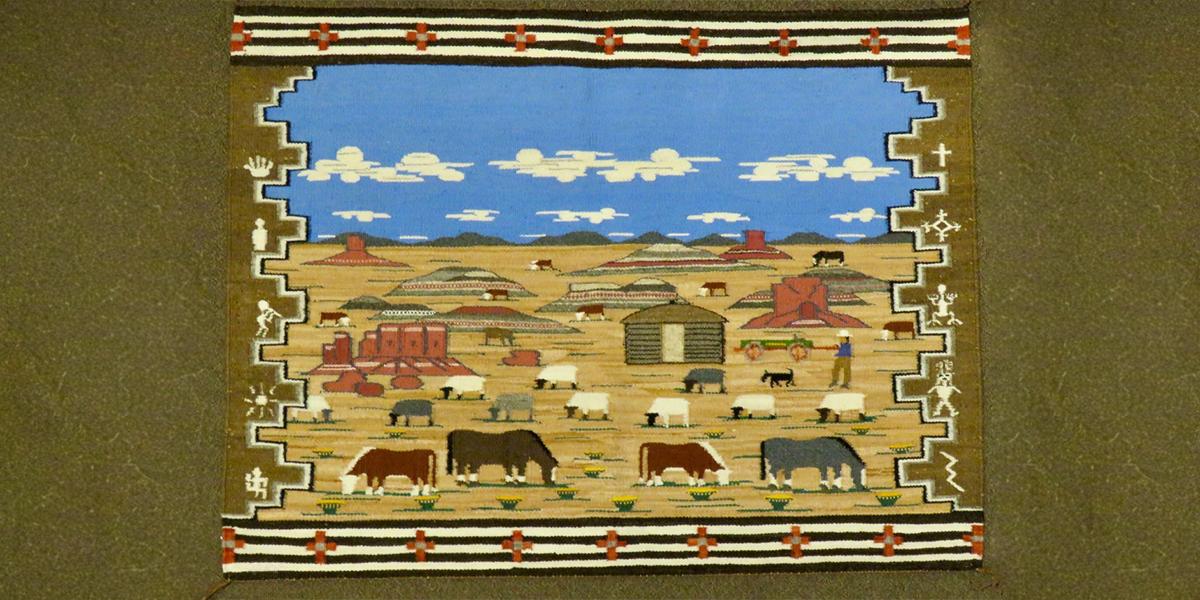woven rug showing landscape with houses and livestock