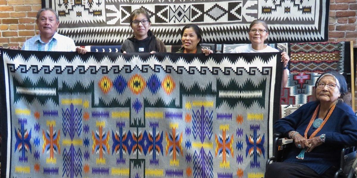 four people holding rug with one woman sitting in wheelchair