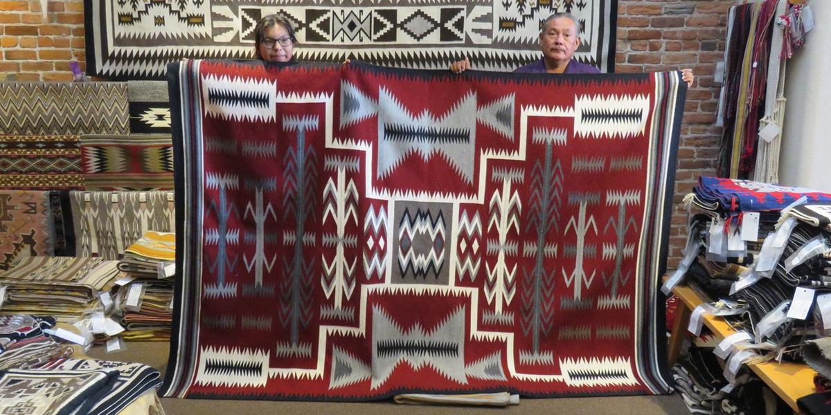 Two people holding rug with geometric designs