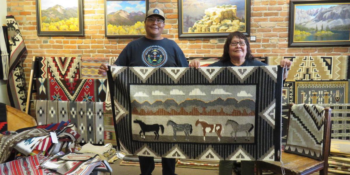 Young man and his mother holding woven rug with mountain and horse design