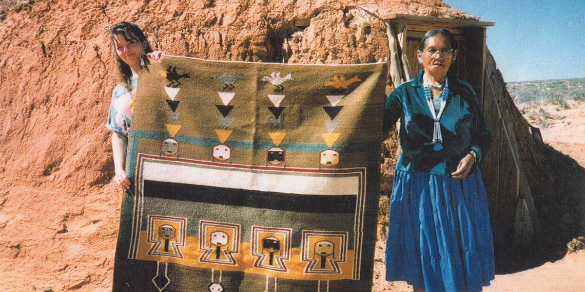two woman outside holding rug with geometric pattern