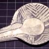 A geometrically patterned black and white ladle made of clay. The right edge of the ladle is slightly more worn down than the left side.