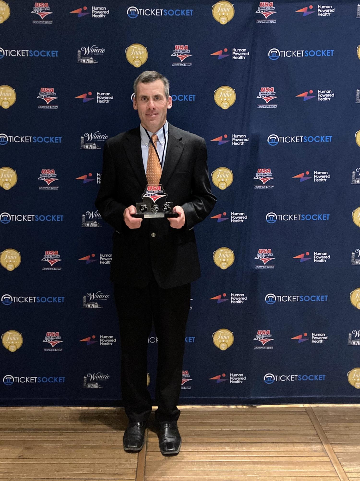 Steve Eles in a suit holding a plaque