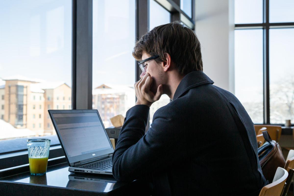 Photo of a student studying on his laptop by a window.