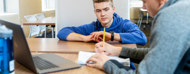 Student helping one student with his work at a desk
