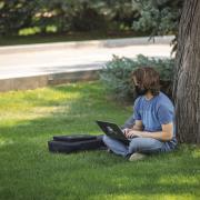 student sitting under a tree studying on his laptop