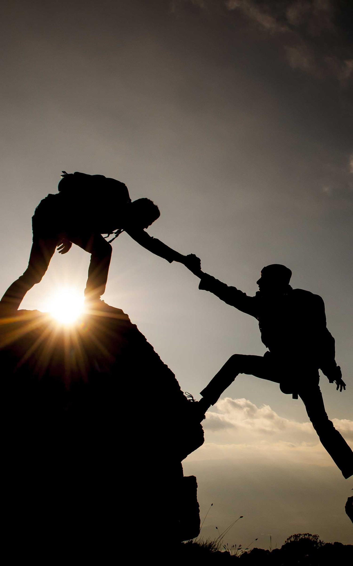 Couple hiking help each other silhouette in mountains