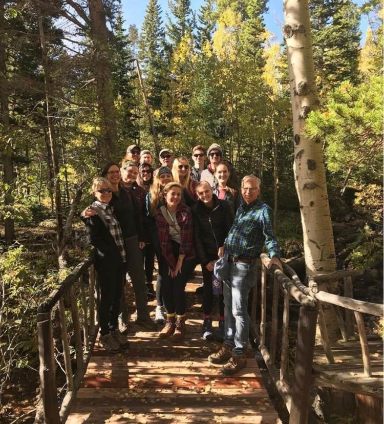 Mike breed with students on a wooded bridge. Aspen trees in background, the class is on a hike