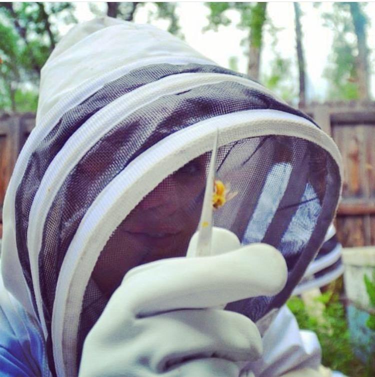 Rachael in a protective bee suit examining a bee on her mask