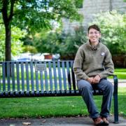 lior sitting on a park bench, greenery in background