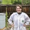 rachel stands in a bee suit, several bee hives in out of focus background