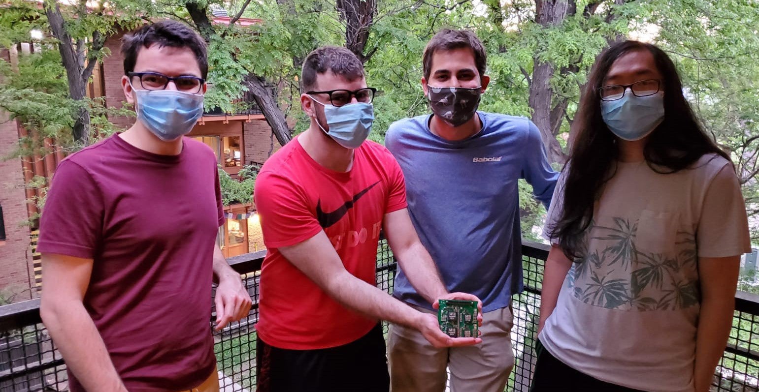 Four masked team members show off their prototype during a testing session at a team member's home. 