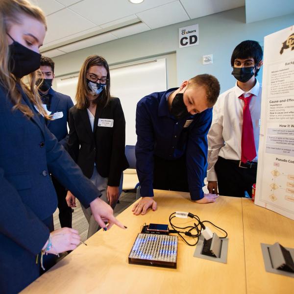 Five students gather around a display to discuss the project