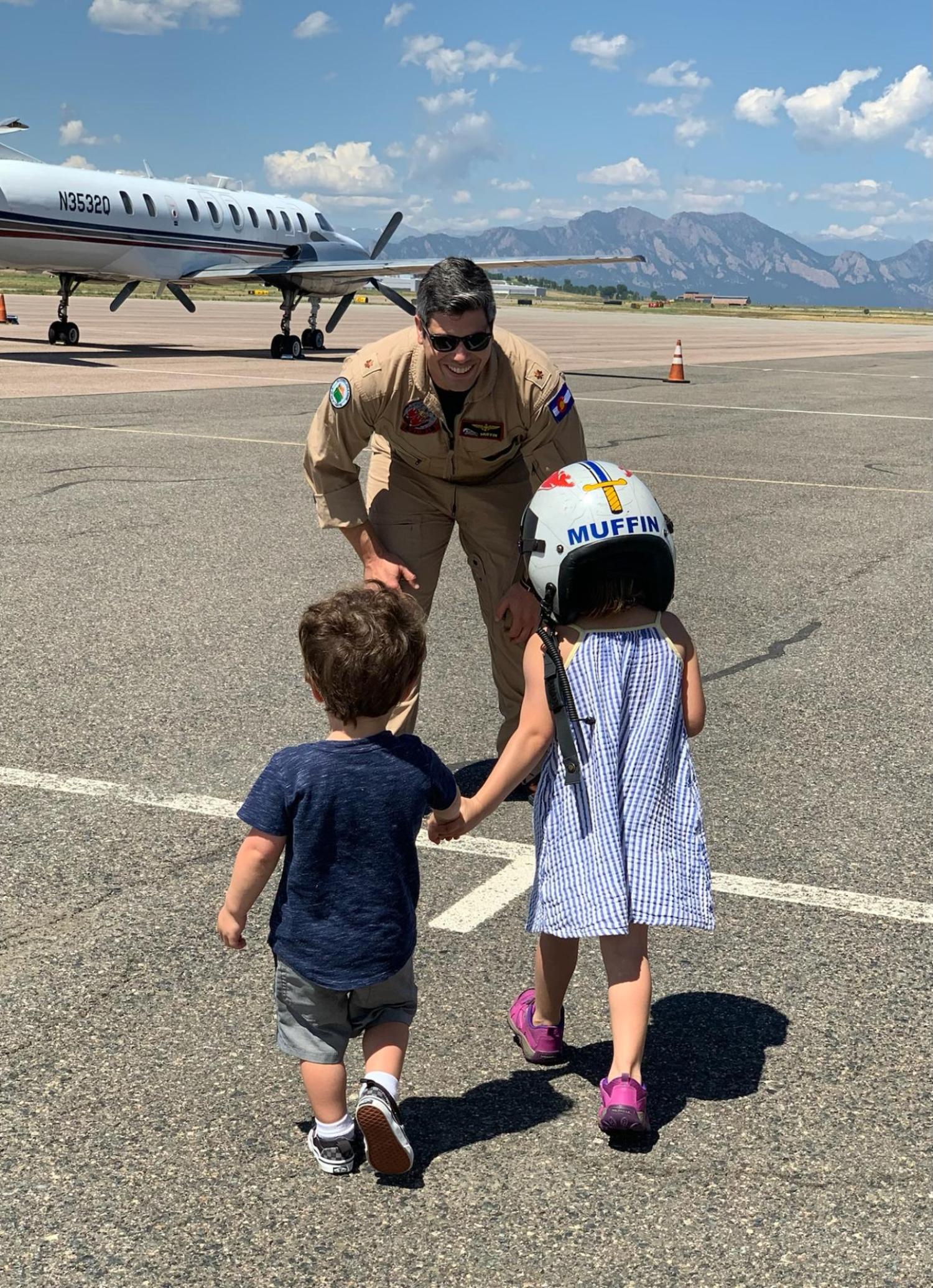 Tom greets his two kids on a runway with a plane in the background