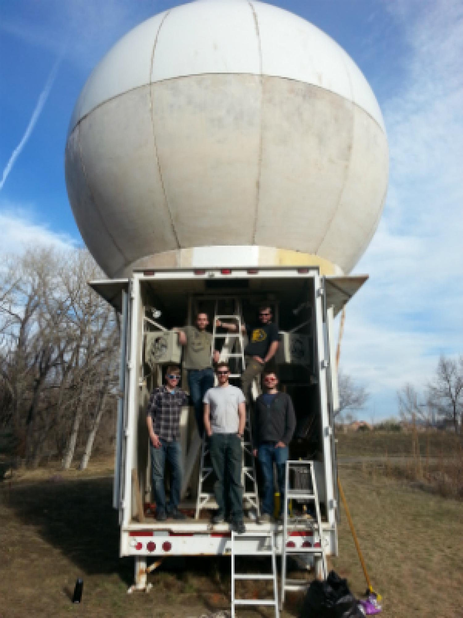 Members of Team Jackalope stand in the doorway of the trailer carrying their radio dish