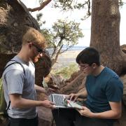 Alex Fosdick and a student look over some data on a laptop at the side of a trail