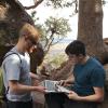 Alex Fosdick and a student look over some data on a laptop at the side of a trail