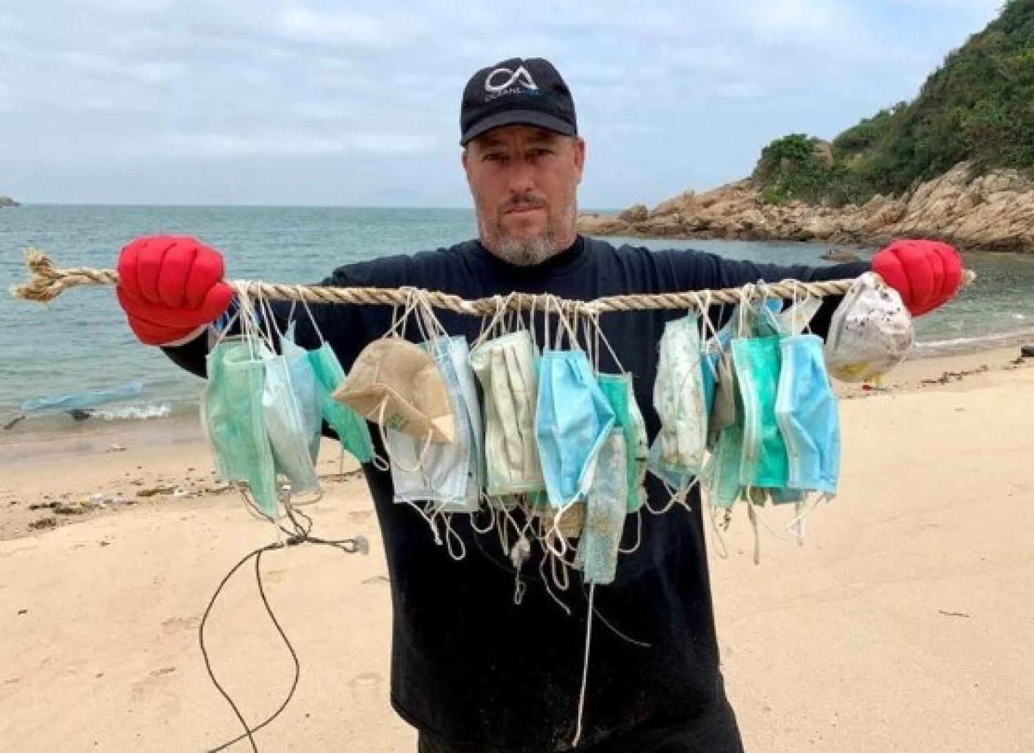 man holding littered masks at the beach