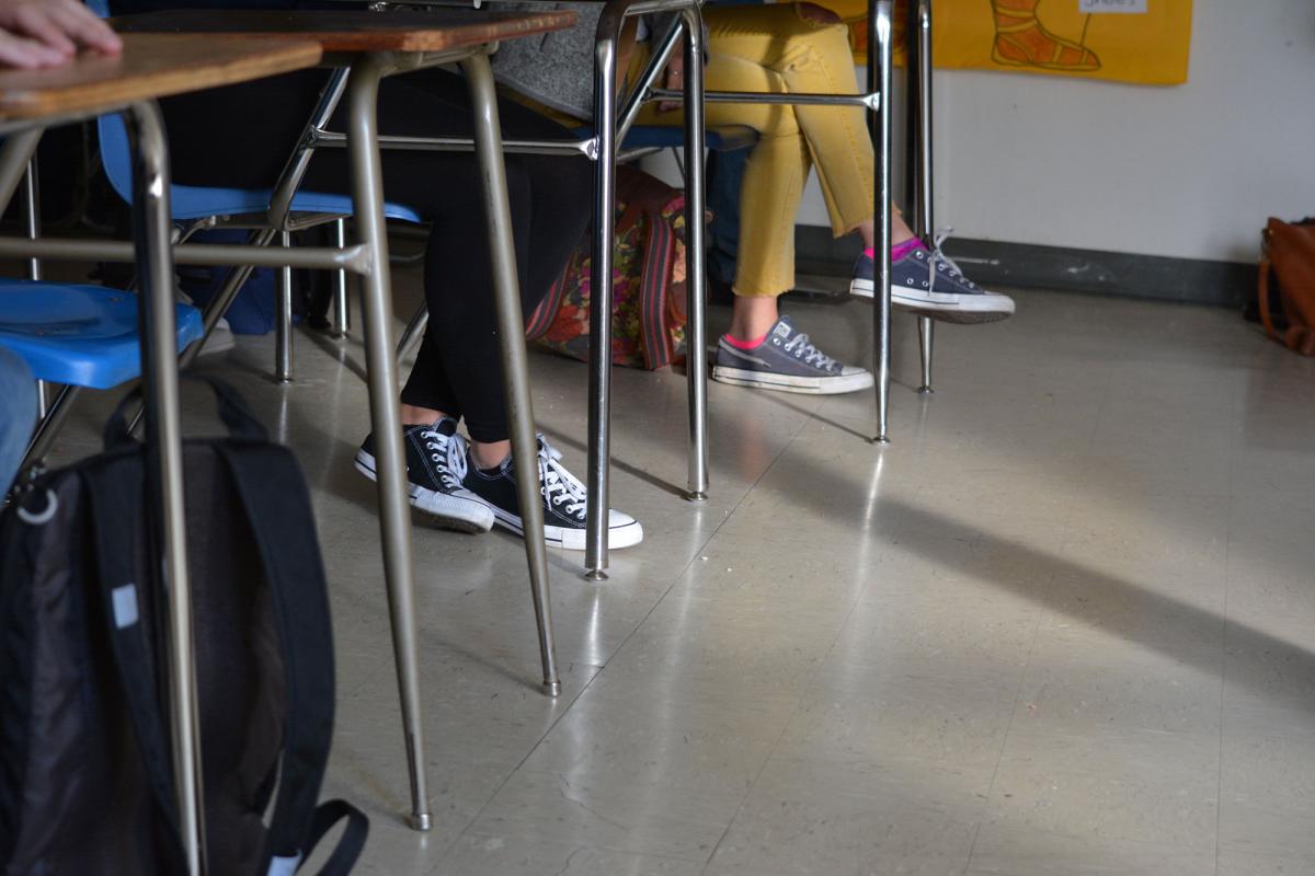 Feet and legs of students sitting at desks in a classroom