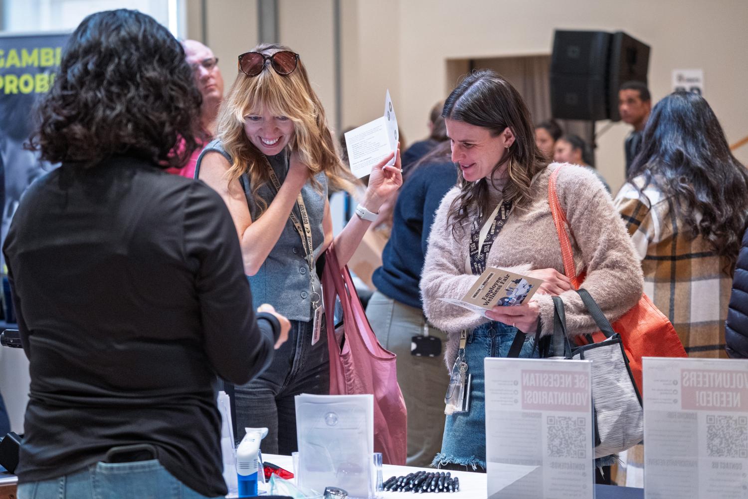 Two women looking at a booth and holding full bags at the 2025 Health and Wellness Fair