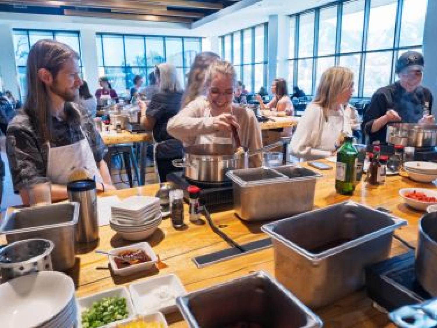 Three people wearing aprons in a kitchen with bowls of ingredients in front of them.