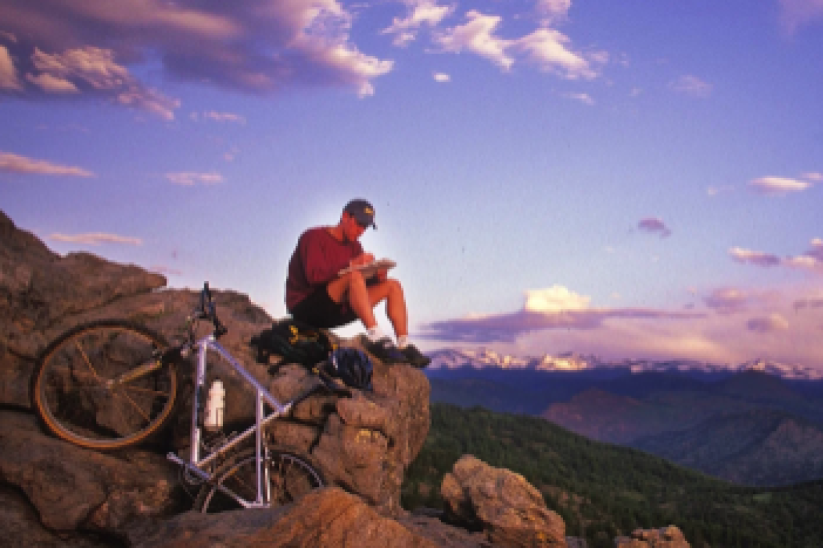 A man sitting on the Flatirons with his mountain bike and journal with the mountains in the background