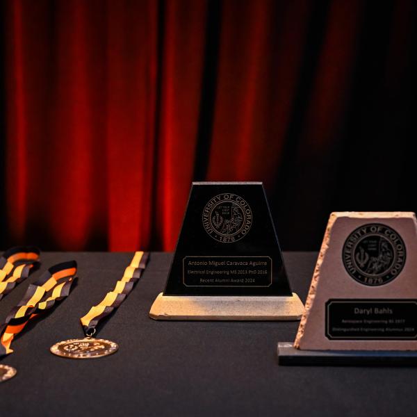 Alumni award plaques and medals arranged on a table in front of a red curtain