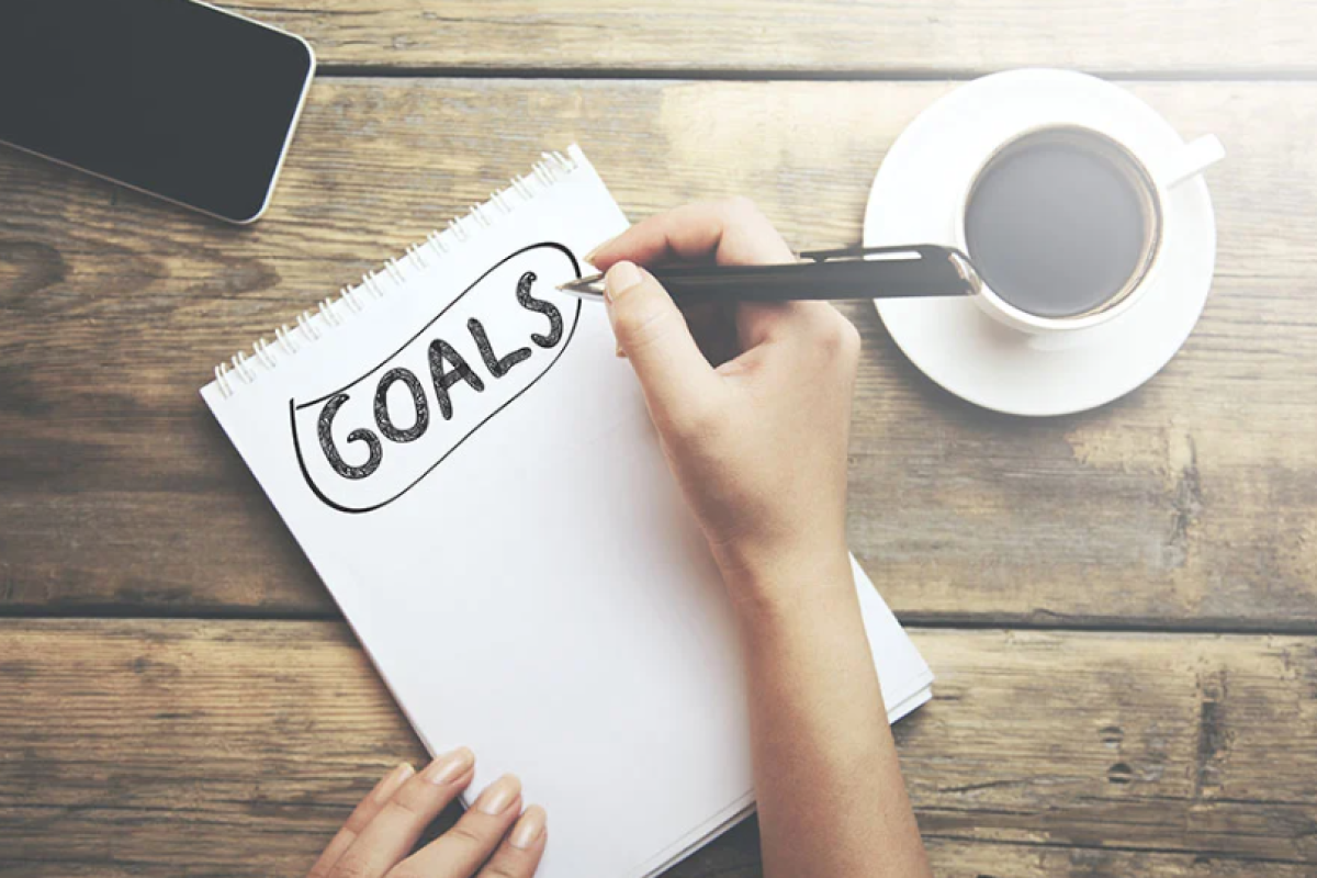 Taking notes on a pad of paper labeled "goals"