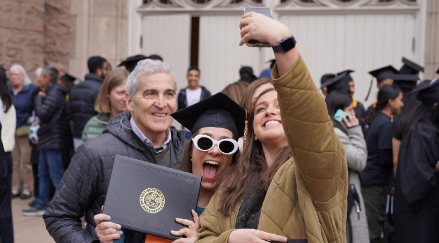 A graduate grins as she takes a selfie outside Macky with friends and family