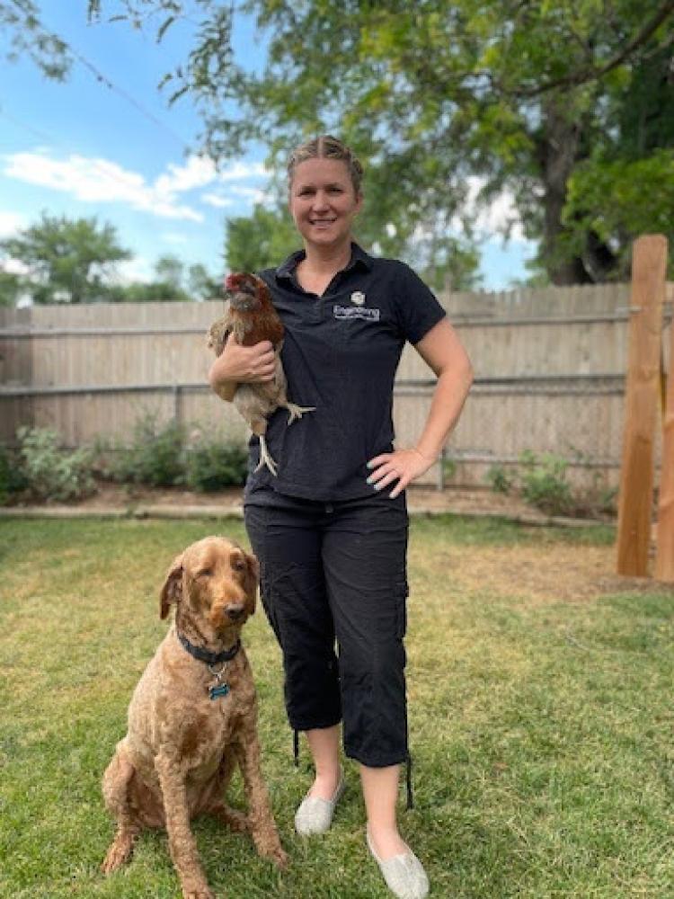 Rowie in her engineering polo, holding a chicken with her dog sitting at her feet