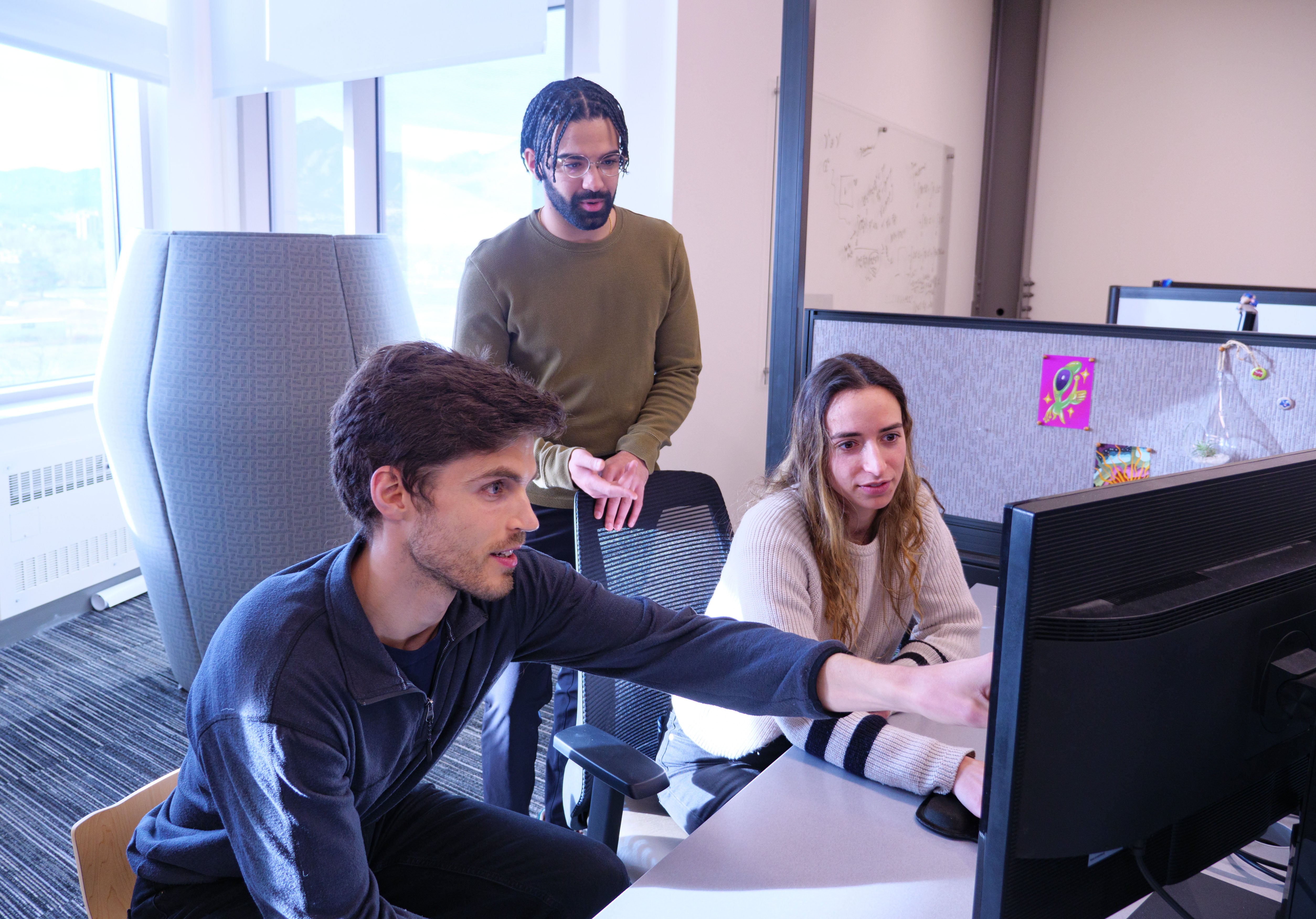 Three aerospace graduate students discuss a project in their office space