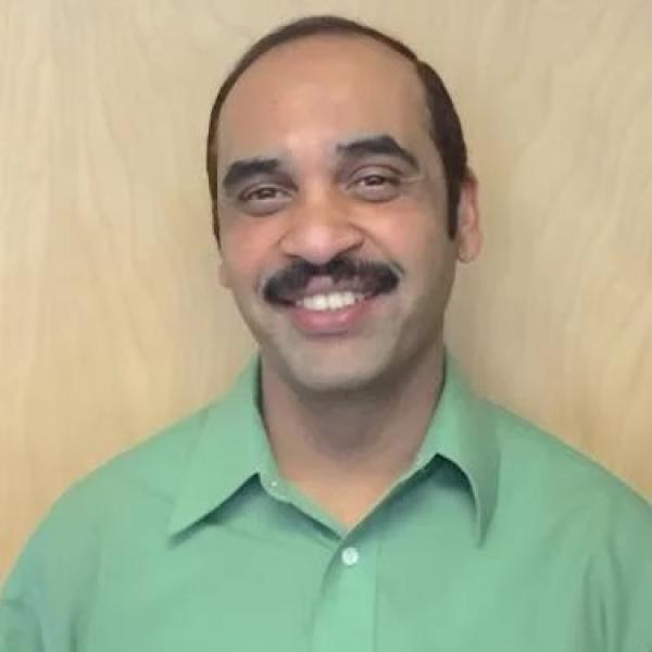 East Indian man with receding dark hair and moustache wearing a bright green button up shirt