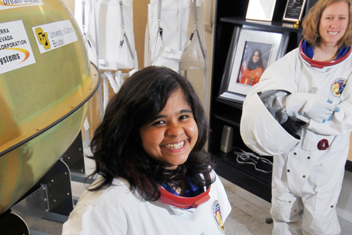 Two people in spacesuits smiles at the camera