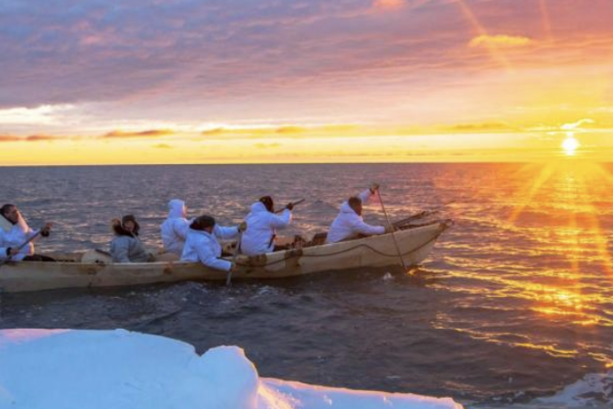 A canoe with people paddling in the Arctic at sunset