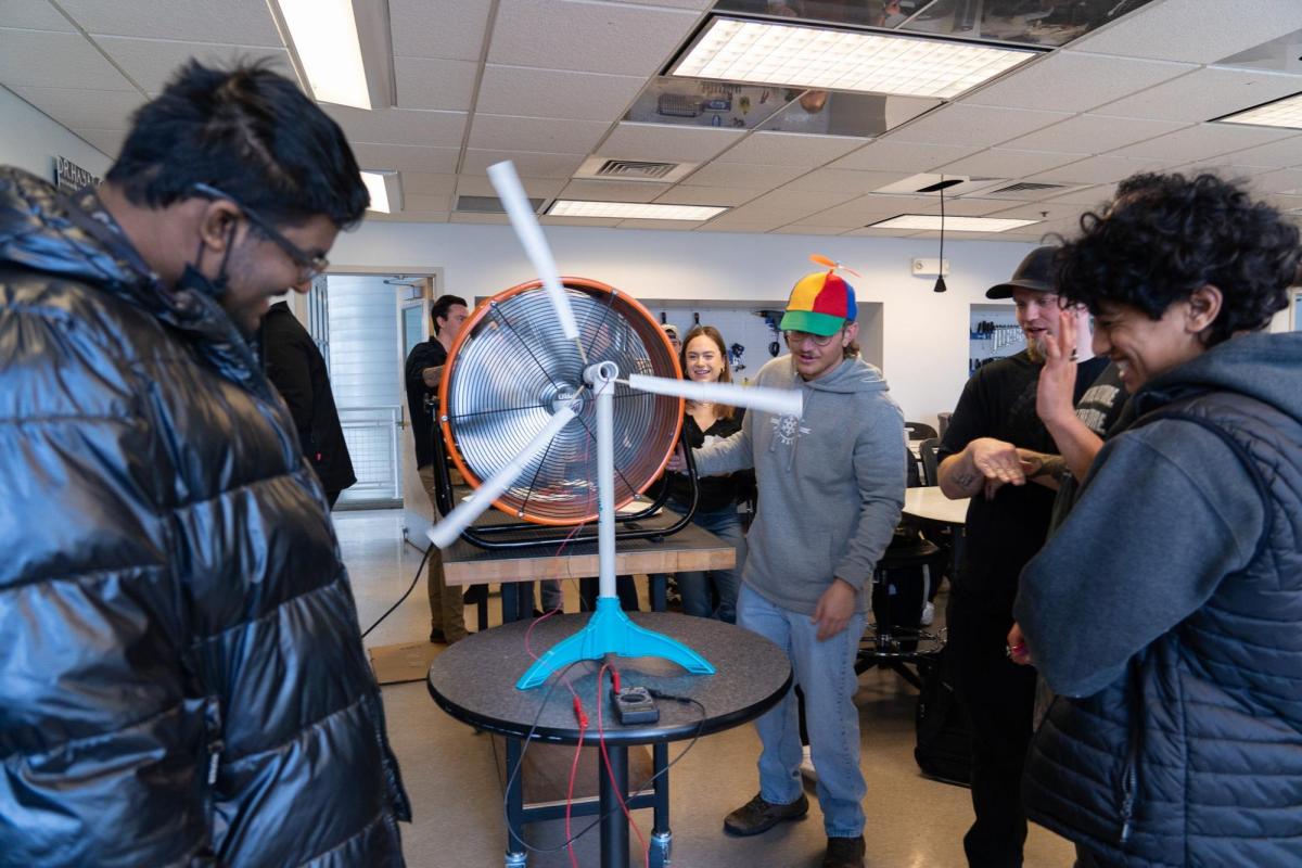 A Wind Team member in a colorful propeller beanie operates a model turbine at an outreach event