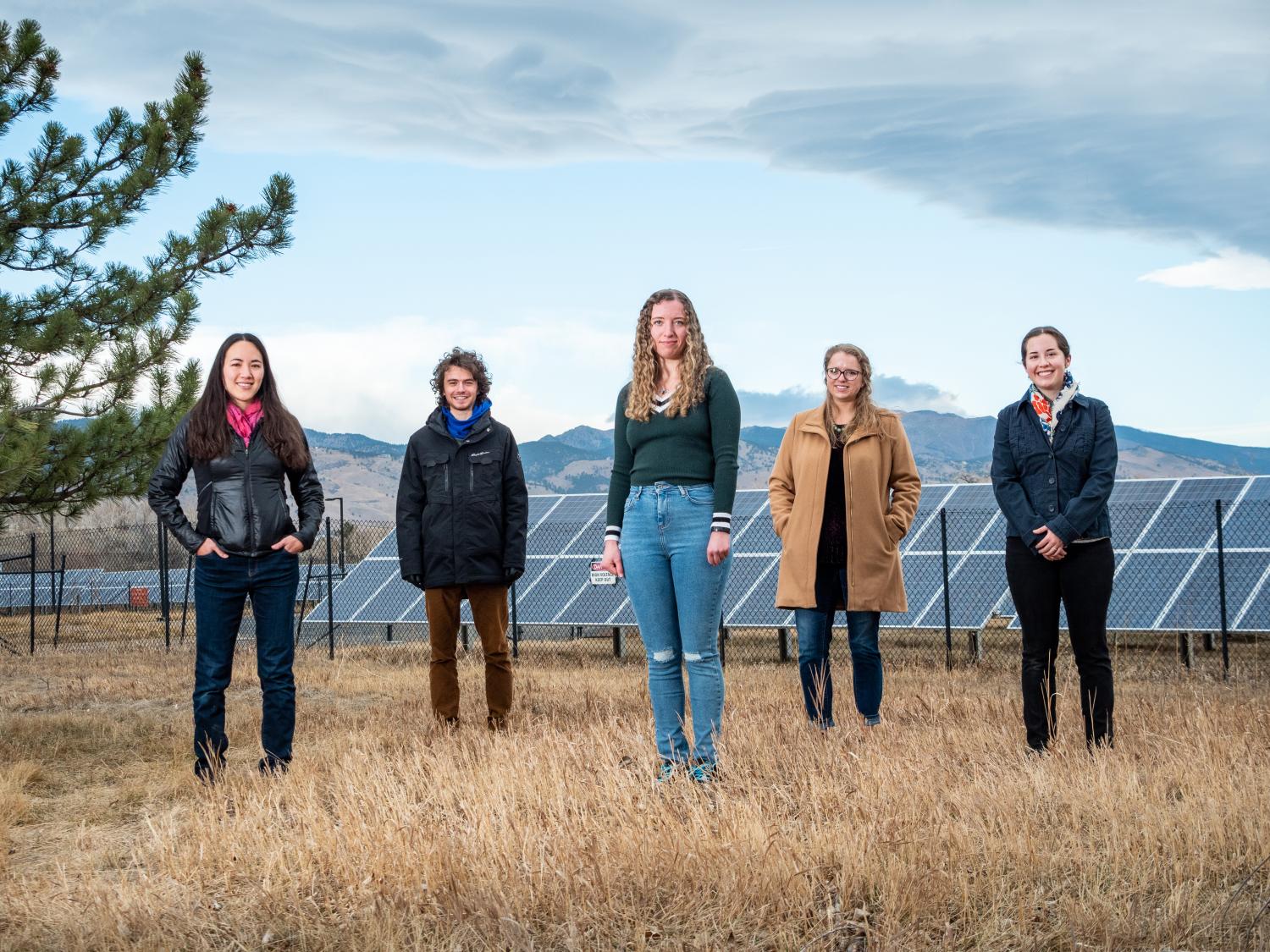 Kyri Baker and research team standing in field with solar panels in the background.