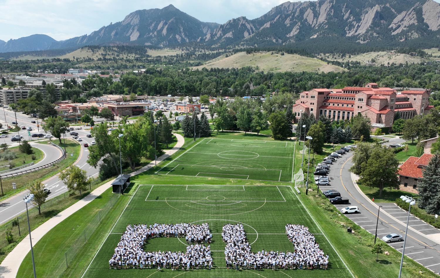 The incoming class for fall 2022 forms the letters CU on the Kittredge Field with the Flatirons in the background in this aerial shot