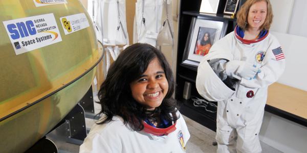 Two people in spacesuits smiles at the camera
