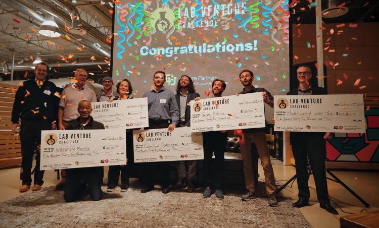 Men and women holding checks made out to their winning startup companies.