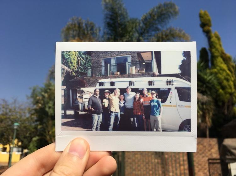 A team member holds a Polaroid of the team standing next to a van.