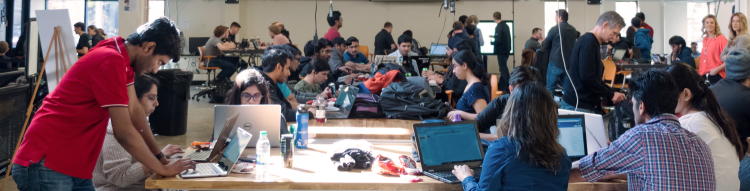 Students in a large room collaborating with each other in front of computers.