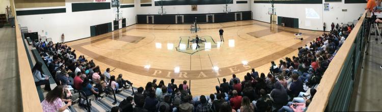 Panoramic shot of Bobby Braun in the high school gym, facing bleachers full of students.
