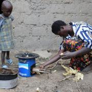 A woman in Rwanda feeds wood into a cookstove as a child looks on.