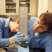 Two students work on the CubeSat in a LASP lab. 