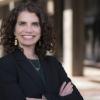 Amy Javernick Will in a black blazer with her arms crossed in front of a blurred building
