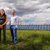Kyri Baker and Bri-Mathias Hodge stand in front of solar panels on the ground and a cloudy sky.