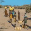 People in Africa dressed in colorful garb carry plastic containers of clean water on their heads.