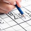 A hand holding a pencil working on a sudoku grid