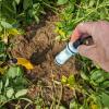 A person holding a soil sensor above a patch of dirt and leaves
